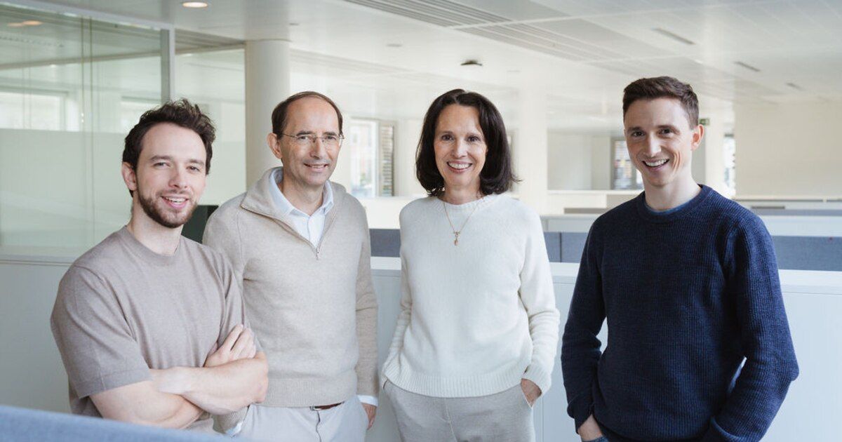 A diverse team of four professionals smiles for a photo in their brightly lit, contemporary office environment. Four smiling colleagues, two men and two women, pose in a modern office space.