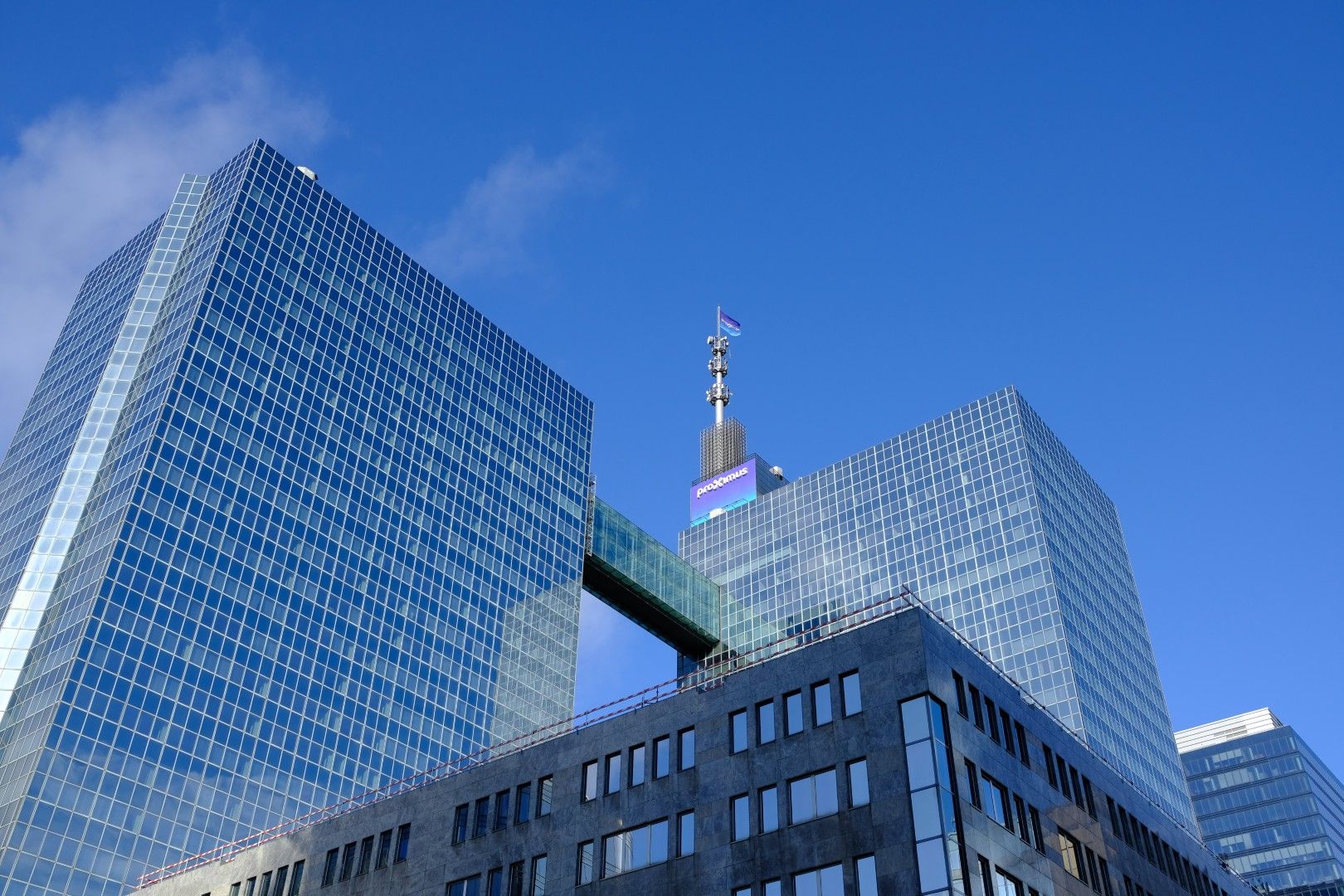 These modern high-rise buildings exemplify contemporary urban architecture and design, reaching towards the sky. Modern glass skyscrapers with a connecting walkway under a clear blue sky.