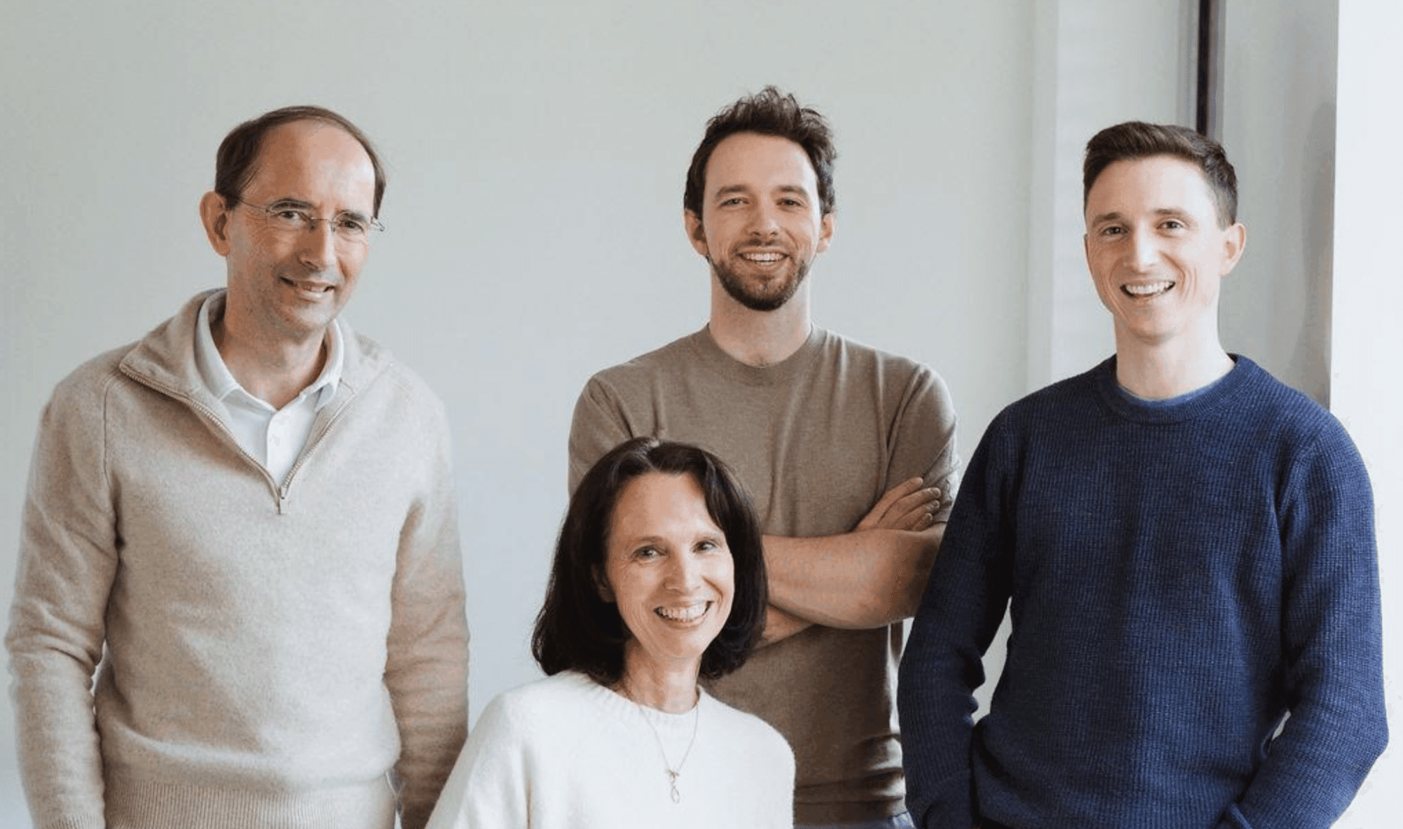 A professional team of four smiles confidently, ready to collaborate and achieve their goals. This group exemplifies unity and forward-thinking. Four smiling team members, three men standing and one woman seated, look forward.