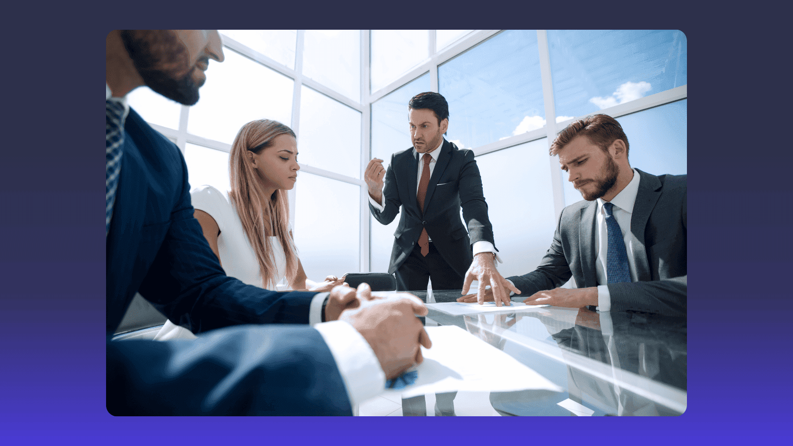 Four business professionals discuss documents around a modern conference table in a bright office.