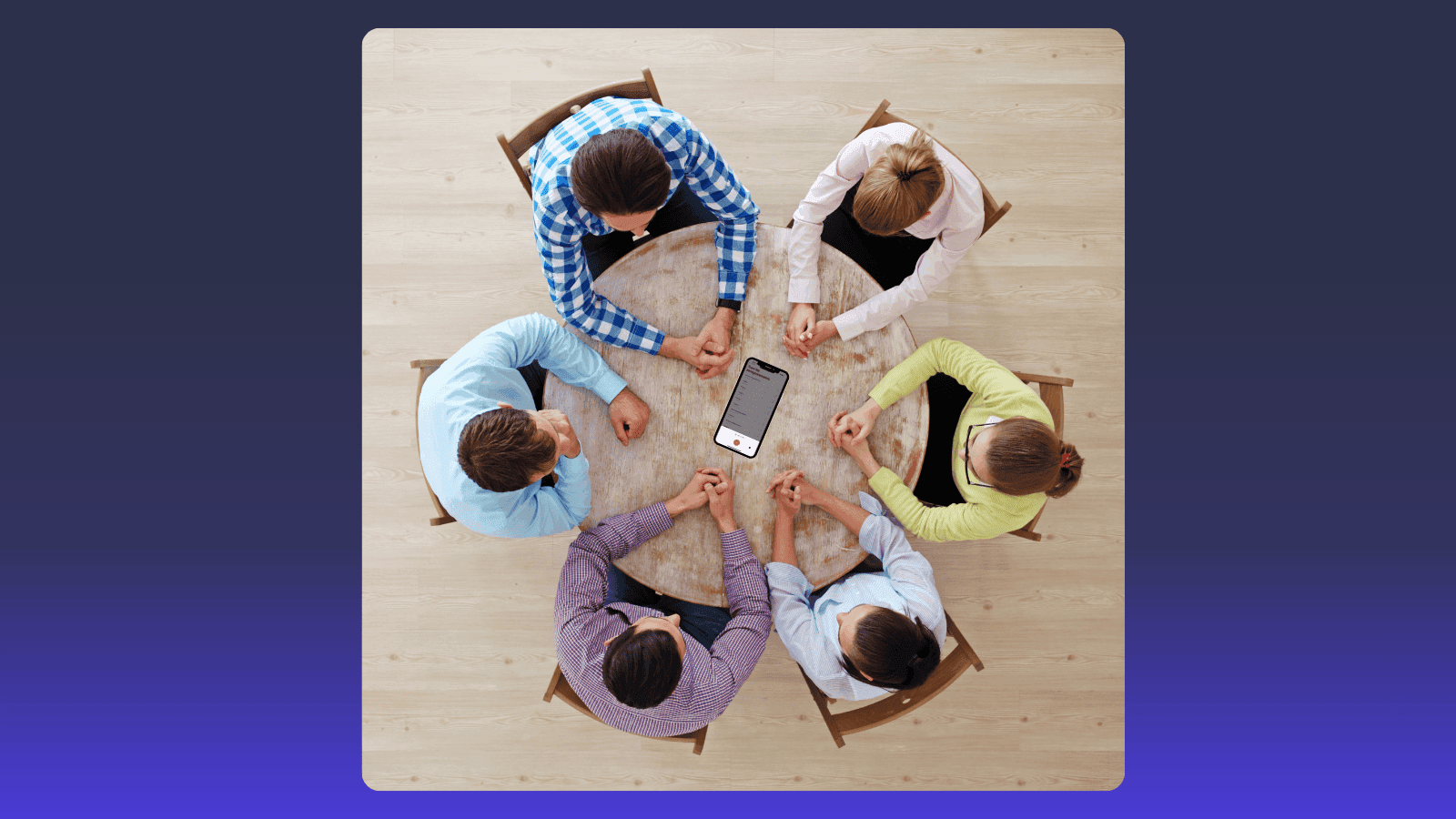 Six people sit around a circular table, intently looking down at a smartphone.