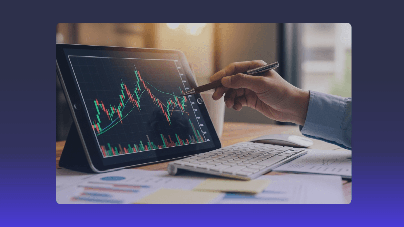 A person's hand uses a stylus on a tablet displaying a dynamic stock market chart.