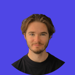 A young man with brown hair and a beard smiles against a blue background.