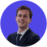 Smiling young man in a dark suit and blue tie against a purple background.