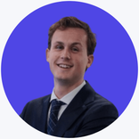 Smiling young man in a dark suit against a blue background.