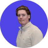 Young man with brown hair wearing a cream quarter-zip sweater on a blue background.