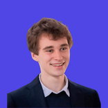 Smiling young man with light brown hair wearing a dark suit jacket and white shirt.