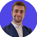 Man with beard, white shirt, and blue suit smiles against a blue background.