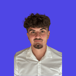 Young man with curly brown hair, goatee, and white shirt against a blue background.