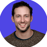 Smiling man with dark hair, beard, and brown sweater on a blue background.