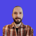 A man with a shaved head and beard wearing a plaid shirt against a blue background.