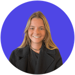 Smiling young woman with long blonde hair wearing a dark jacket on a blue background.